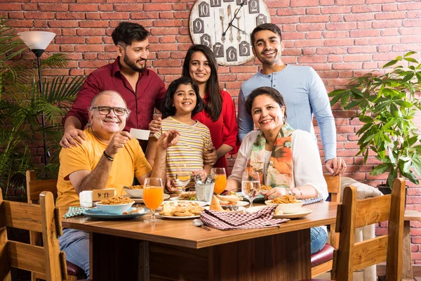 Indian multigenerational Family eating food at dining table at home or restaurant. South Asian grandfather, mother, father and two daughters having meal together