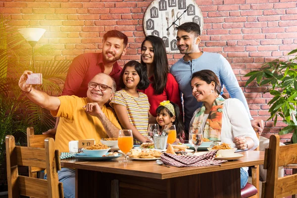 Indian multigenerational Family eating food at dining table at home or restaurant. South Asian grandfather, mother, father and two daughters having meal together