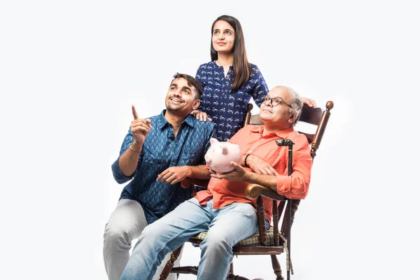 Indian old man or father holding piggy bank with young son and daughter, sitting over rocking chair