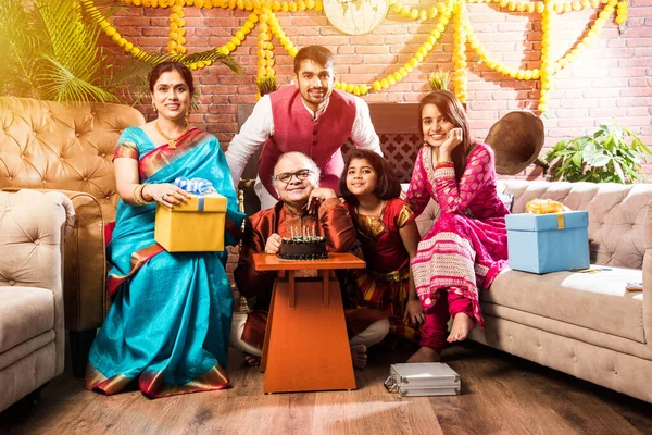 Ailesi olan Hintli yaşlı adam, etnik kıyafetler giyerken pastaya mum üfleyerek doğum gününü kutluyor.