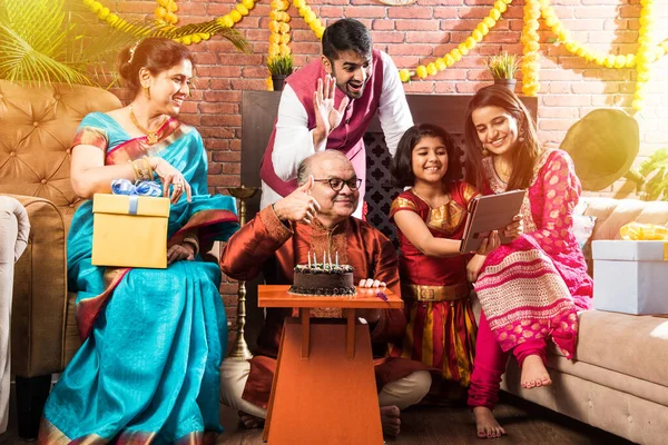 Ailesi olan Hintli yaşlı adam, etnik kıyafetler giyerken pastaya mum üfleyerek doğum gününü kutluyor.