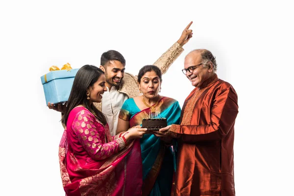 Indian senior woman with Family celebrating birthday by blowing candles on cake while wearing ethnic wear