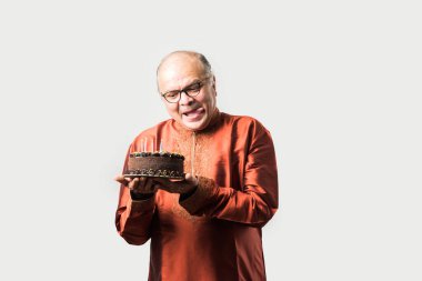 Hintli yaşlı adam, etnik giysiler giyerken pastaya mum üfleyerek doğum gününü kutluyor.