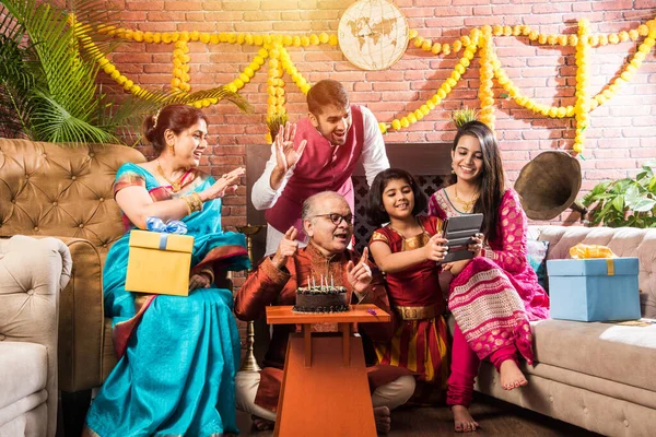 Ailesi olan Hintli yaşlı adam, etnik kıyafetler giyerken pastaya mum üfleyerek doğum gününü kutluyor.