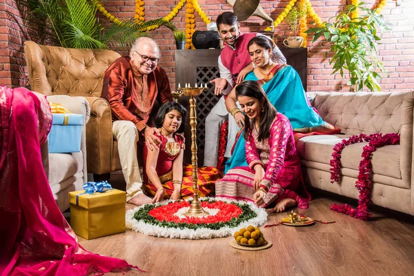 Happy Indian Family Celebrating Ganesh Festival or Chaturthi - Welcoming or performing Pooja and eating sweets in traditional wear at home decorated with Marigold Flowers