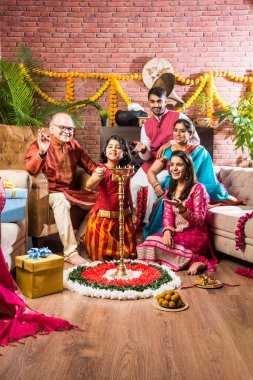 Happy Indian Family Celebrating Ganesh Festival or Chaturthi - Welcoming or performing Pooja and eating sweets in traditional wear at home decorated with Marigold Flowers clipart