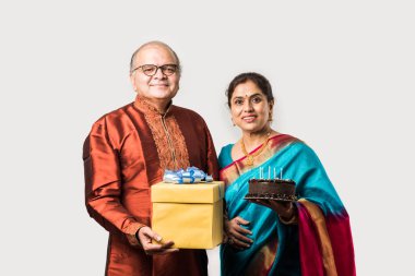 Hintli neşeli yaşlı çift geleneksel giysiler giyerken çikolatalı pastayla doğum gününü kutluyor.