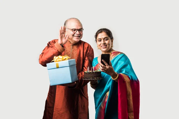 Indian cheerful old couple celebrating birthday with chocolate cake while wearing ethnic traditional cloths