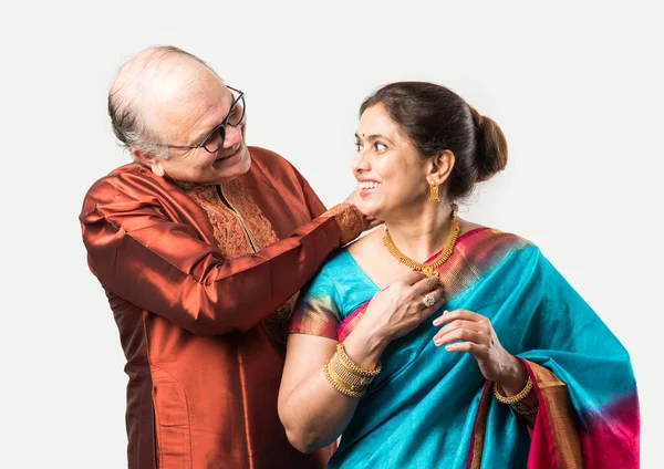 Indian old man tying or presenting gold necklace to his beautiful wife on birthday, valentine day, anniversary or Diwali festival