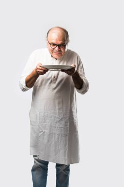 Yaşlı ya da yaşlı Hintli bir adam kaşıkla çatal kullanarak boş beyaz tabak ya da kâseden yemek yiyor. Beyaz arka planda farklı ifadelerle tek başına duruyor.