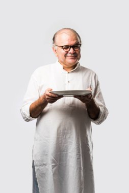 Yaşlı ya da yaşlı Hintli bir adam kaşıkla çatal kullanarak boş beyaz tabak ya da kâseden yemek yiyor. Beyaz arka planda farklı ifadelerle tek başına duruyor.