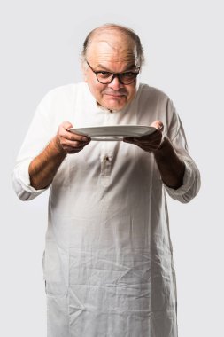 Yaşlı ya da yaşlı Hintli bir adam kaşıkla çatal kullanarak boş beyaz tabak ya da kâseden yemek yiyor. Beyaz arka planda farklı ifadelerle tek başına duruyor.