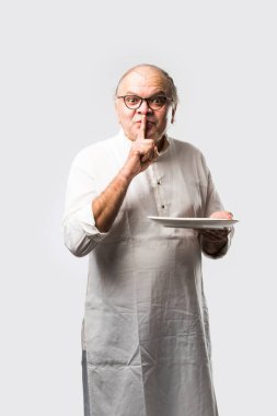 Yaşlı ya da yaşlı Hintli bir adam kaşıkla çatal kullanarak boş beyaz tabak ya da kâseden yemek yiyor. Beyaz arka planda farklı ifadelerle tek başına duruyor.