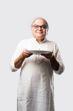 Yaşlı ya da yaşlı Hintli bir adam kaşıkla çatal kullanarak boş beyaz tabak ya da kâseden yemek yiyor. Beyaz arka planda farklı ifadelerle tek başına duruyor.