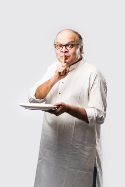 Yaşlı ya da yaşlı Hintli bir adam kaşıkla çatal kullanarak boş beyaz tabak ya da kâseden yemek yiyor. Beyaz arka planda farklı ifadelerle tek başına duruyor.