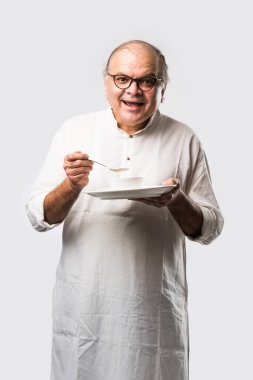 Yaşlı ya da yaşlı Hintli bir adam kaşıkla çatal kullanarak boş beyaz tabak ya da kâseden yemek yiyor. Beyaz arka planda farklı ifadelerle tek başına duruyor.