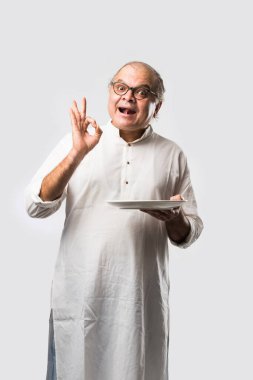 Yaşlı ya da yaşlı Hintli bir adam kaşıkla çatal kullanarak boş beyaz tabak ya da kâseden yemek yiyor. Beyaz arka planda farklı ifadelerle tek başına duruyor.