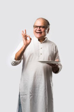 Yaşlı ya da yaşlı Hintli bir adam kaşıkla çatal kullanarak boş beyaz tabak ya da kâseden yemek yiyor. Beyaz arka planda farklı ifadelerle tek başına duruyor.