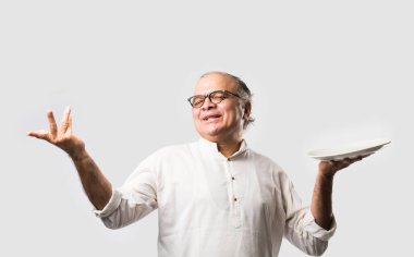 Yaşlı ya da yaşlı Hintli bir adam kaşıkla çatal kullanarak boş beyaz tabak ya da kâseden yemek yiyor. Beyaz arka planda farklı ifadelerle tek başına duruyor.