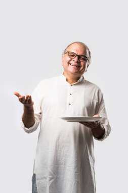 Yaşlı ya da yaşlı Hintli bir adam kaşıkla çatal kullanarak boş beyaz tabak ya da kâseden yemek yiyor. Beyaz arka planda farklı ifadelerle tek başına duruyor.