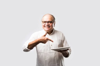 Yaşlı ya da yaşlı Hintli bir adam kaşıkla çatal kullanarak boş beyaz tabak ya da kâseden yemek yiyor. Beyaz arka planda farklı ifadelerle tek başına duruyor.