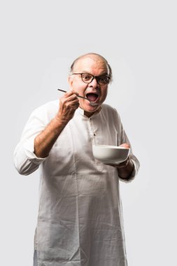 Yaşlı ya da yaşlı Hintli bir adam kaşıkla çatal kullanarak boş beyaz tabak ya da kâseden yemek yiyor. Beyaz arka planda farklı ifadelerle tek başına duruyor.