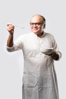Yaşlı ya da yaşlı Hintli bir adam kaşıkla çatal kullanarak boş beyaz tabak ya da kâseden yemek yiyor. Beyaz arka planda farklı ifadelerle tek başına duruyor.