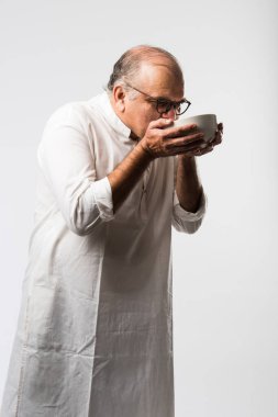 Yaşlı ya da yaşlı Hintli bir adam kaşıkla çatal kullanarak boş beyaz tabak ya da kâseden yemek yiyor. Beyaz arka planda farklı ifadelerle tek başına duruyor.