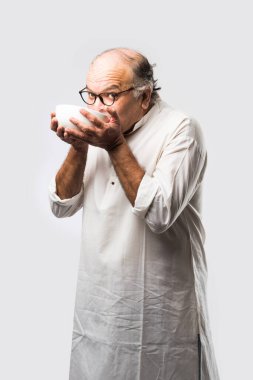 Yaşlı ya da yaşlı Hintli bir adam kaşıkla çatal kullanarak boş beyaz tabak ya da kâseden yemek yiyor. Beyaz arka planda farklı ifadelerle tek başına duruyor.