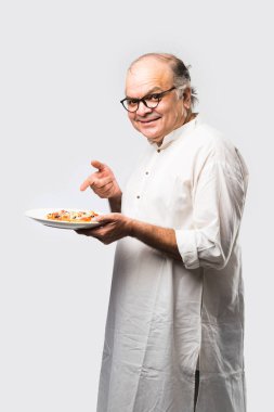 Beyaz arka planda tek başına dururken pizza yiyen yaşlı ya da yaşlı Hintli bir adam.