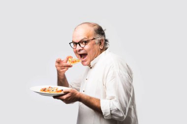 Beyaz arka planda tek başına dururken pizza yiyen yaşlı ya da yaşlı Hintli bir adam.