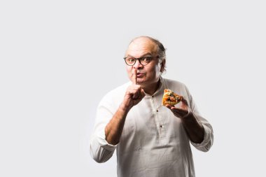 Beyaz arka planda tek başına dururken pizza yiyen yaşlı ya da yaşlı Hintli bir adam.