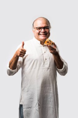 Beyaz arka planda tek başına dururken pizza yiyen yaşlı ya da yaşlı Hintli bir adam.
