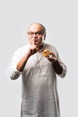 Beyaz arka planda tek başına dururken pizza yiyen yaşlı ya da yaşlı Hintli bir adam.