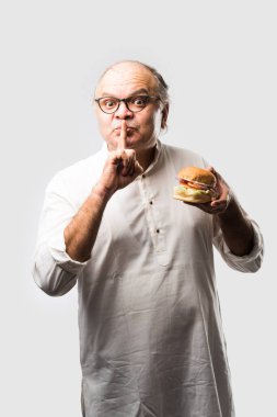 Hint ihtiyarı hamburger ya da mango suyu ya da soğuk içecek ile hamburger yiyor.