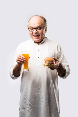 Hint ihtiyarı hamburger ya da mango suyu ya da soğuk içecek ile hamburger yiyor.