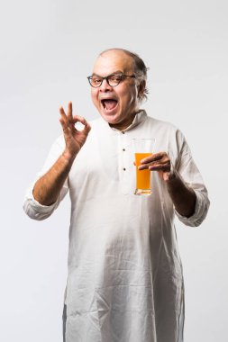 Mutlu yaşlı Hintli adam içiyor veya elinde bir bardak taze portakal ya da mango suyu tutuyor.
