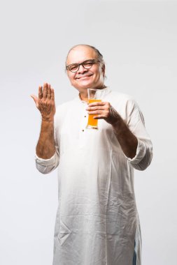 Mutlu yaşlı Hintli adam içiyor veya elinde bir bardak taze portakal ya da mango suyu tutuyor.