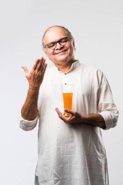 Mutlu yaşlı Hintli adam içiyor veya elinde bir bardak taze portakal ya da mango suyu tutuyor.