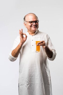 Mutlu yaşlı Hintli adam içiyor veya elinde bir bardak taze portakal ya da mango suyu tutuyor.