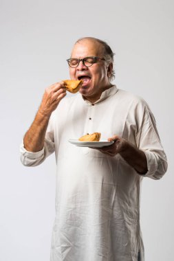 Hintli yaşlı adam ya da kıdemli adam samosa ya da sebzeli börek yiyor.