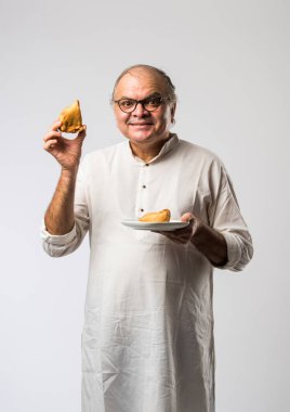 Hintli yaşlı adam ya da kıdemli adam samosa ya da sebzeli börek yiyor.