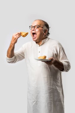 Hintli yaşlı adam ya da kıdemli adam samosa ya da sebzeli börek yiyor.