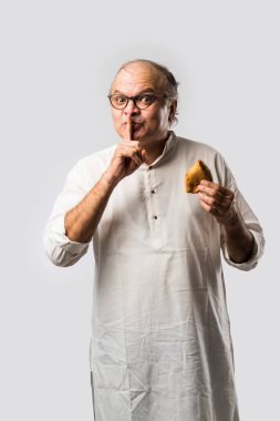 Hintli yaşlı adam ya da kıdemli adam samosa ya da sebzeli börek yiyor.