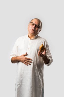 Hintli yaşlı adam ya da kıdemli adam samosa ya da sebzeli börek yiyor.