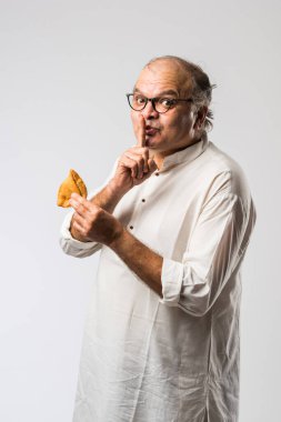 Hintli yaşlı adam ya da kıdemli adam samosa ya da sebzeli börek yiyor.