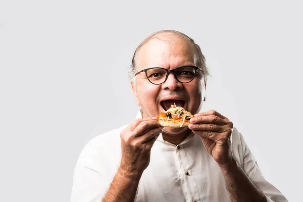 Indian asian senior or old man eating pizza while standing isolated against white background