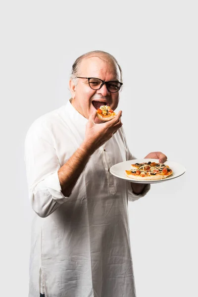 Indian asian senior or old man eating pizza while standing isolated against white background