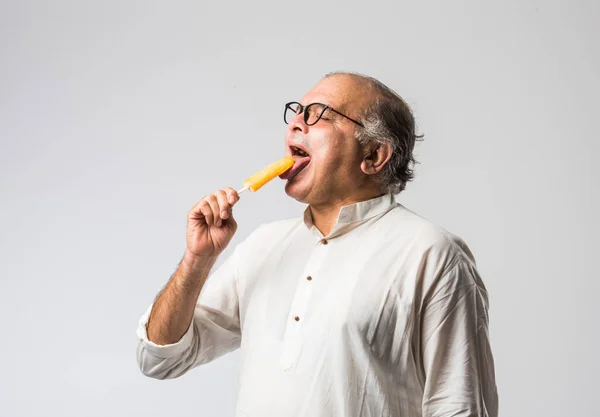 Indian Old man eating chocolate Ice cream in cone or mango candy bar