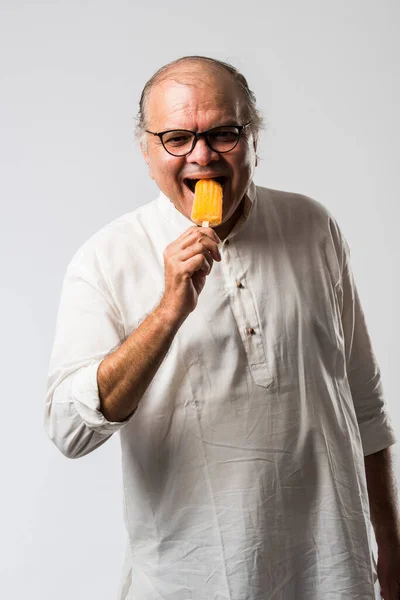 Indian Old man eating chocolate Ice cream in cone or mango candy bar